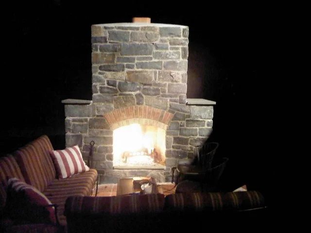 Outdoor stone fireplace glowing at night with seating around it