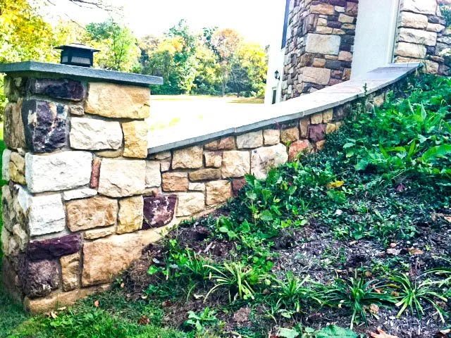 Fieldstone pillar and capped retaining wall beside a planting bed
